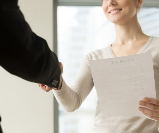 Female business leader holding contract document and shaking hand with colleague before or after negotiation. Businesswoman concluding agreement, starting partnership, accepting offer. Close up view
